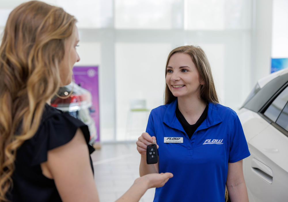A Flow employee passing a car key to a customer inside the dealership