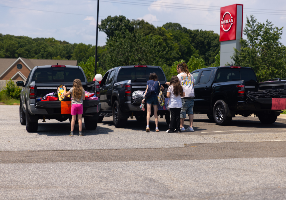 A group of people looking through backpacks in the beds of trucks parked outside Flow Nissan of Statesville