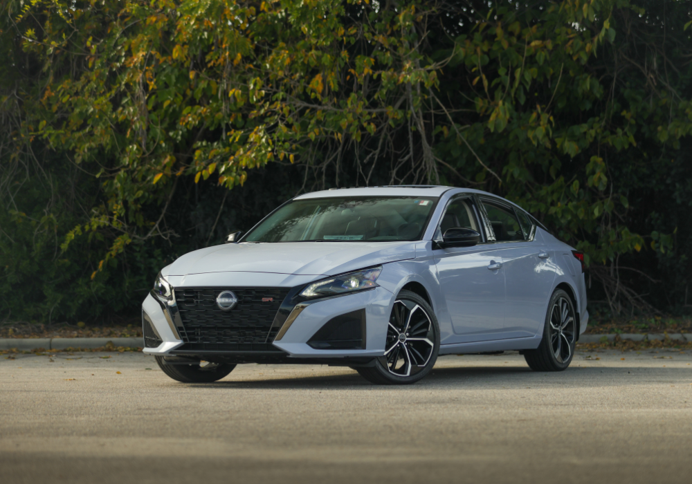 White 2025 Nissan Altima for sale parked on a paved surface with trees in the background